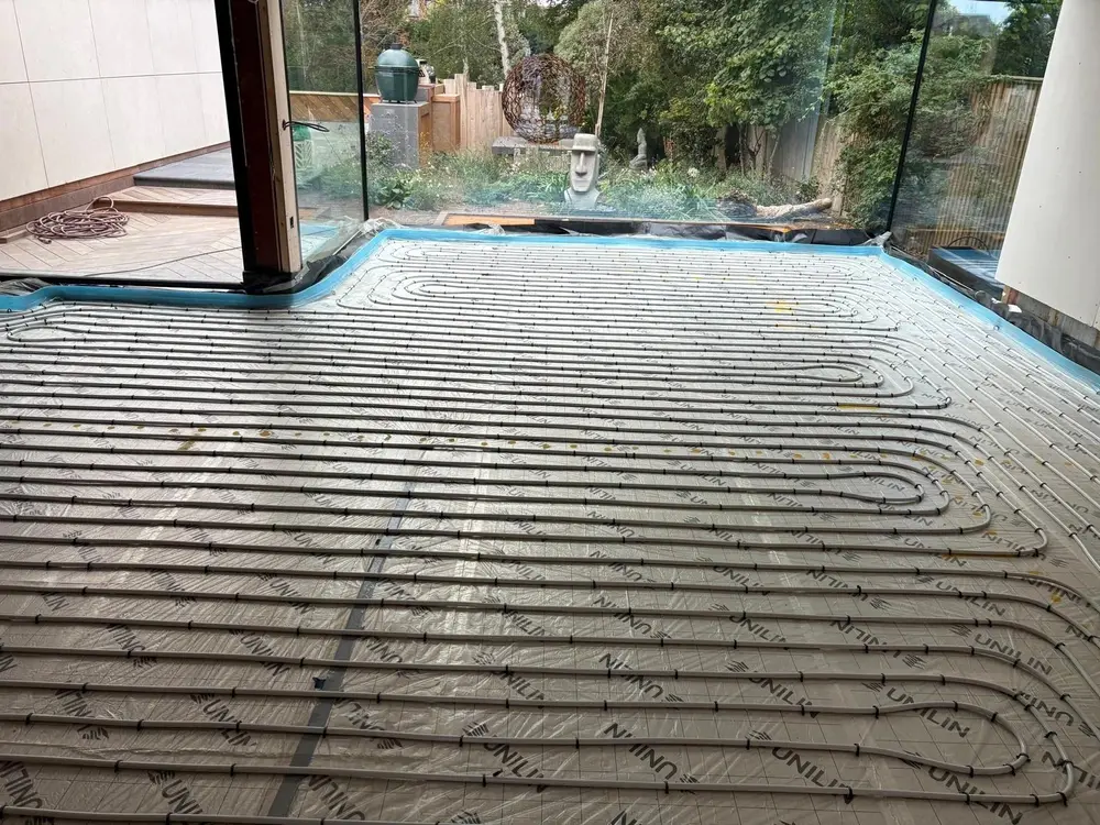 Wet underfloor heating pipe laid in a close, even pattern over insulation across the whole floor of a contemporary extension with full height glazing.