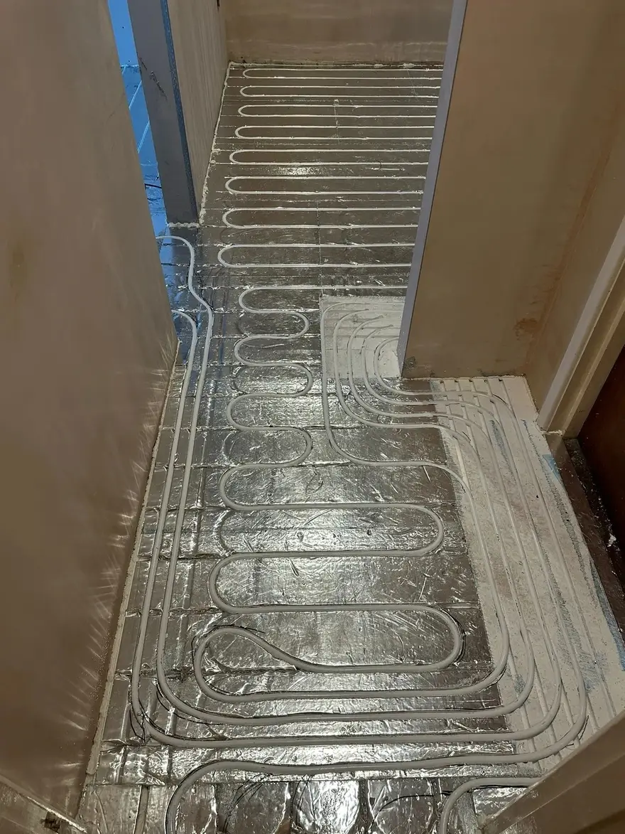 A hallway and rooms in an existing house with plastered walls, the floor covered in silver grooved panels with underfloor heating pipe pressed into the channels and running through the doorways.